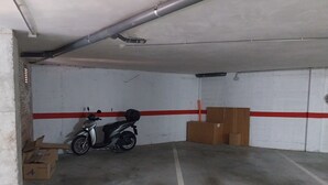 Uma garagem de estacionamento com uma scooter estacionada perto de uma parede, caixas empilhadas na parede e um chão de concreto com linhas brancas.