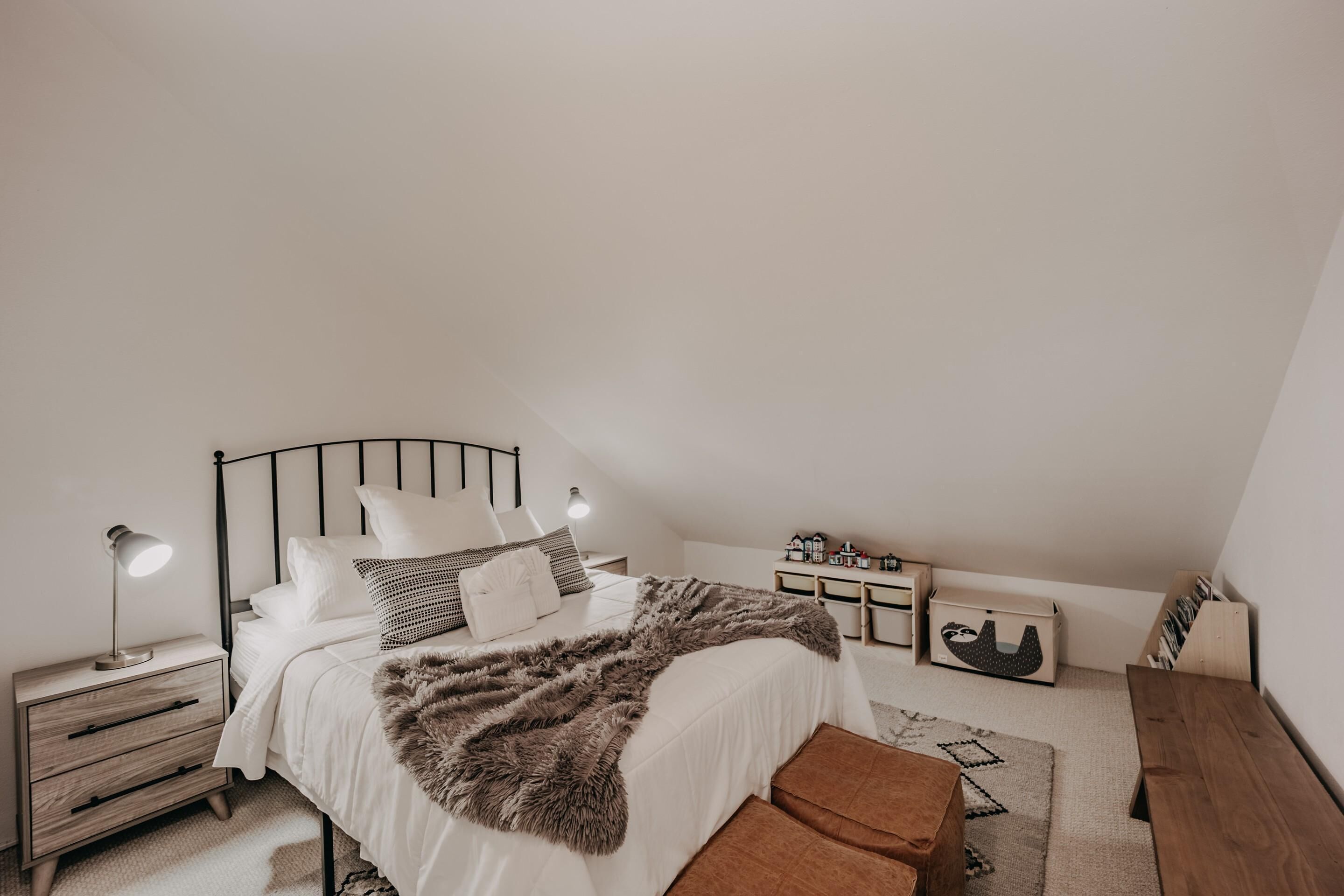 Une chambre à coucher comprenant un lit, des tables de chevet, une commode, un banc et un petit meuble en bois.