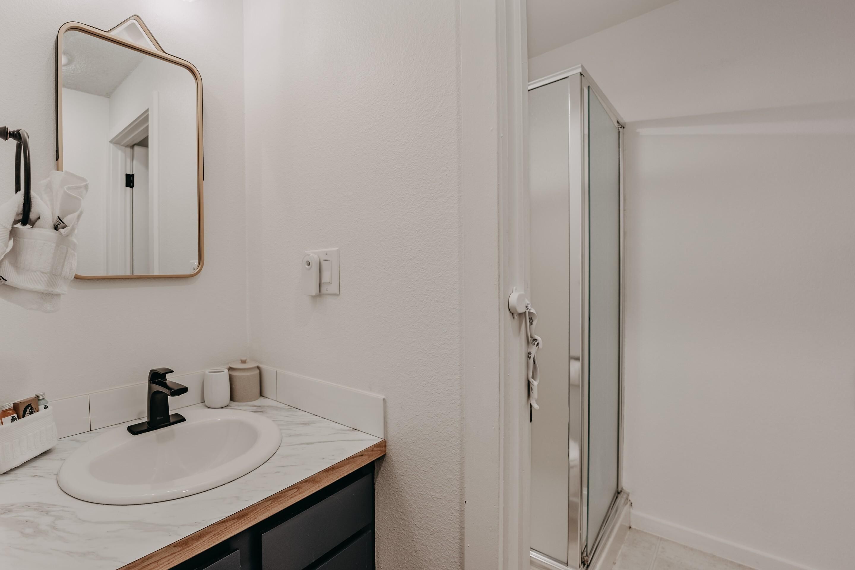 A bathroom with a white sink, black faucet, and a wooden countertop. There is a mirror above the sink and a shower door to the right.