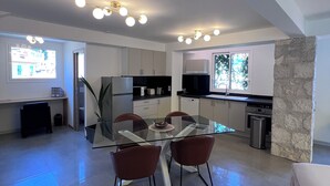 A modern kitchen with a stone accent wall, a dining area with a glass table and red chairs, and a recessed ceiling light fixture. - Ground floor of a house, in a quiet location in the hills above Nice, a 1/4 h from downtown. (Nice)