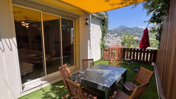 A patio with a table and chairs, a yellow awning, and a view of a cityscape. - Ground floor of a house, in a quiet location in the hills above Nice, a 1/4 h from downtown. (Nice)
