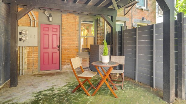An outdoor patio with a brick wall, a pink door, and a black fence.