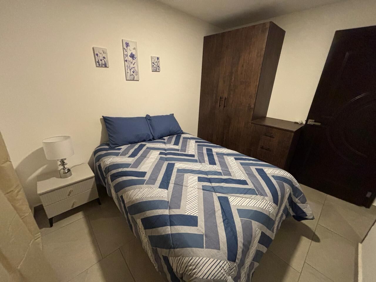 Un dormitori amb un llit, una nit, una armariada de fusta i una porta.