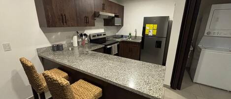 Una cocina moderna con armarios de madera oscura, encimera de granito y una isla integrada con taburetes de bar.