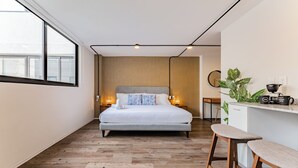 Een moderne slaapkamer met een groot bed, nachtkastjes met lampen, een klein bureau en een potplant.