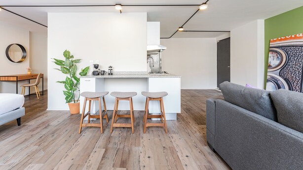 Een moderne keuken met een centraal eiland, houten krukken en een eethoek met tafel en stoelen.