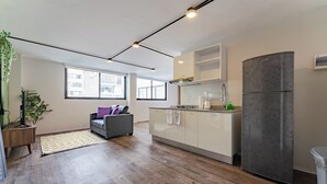 Een moderne keuken met een grijze koelkast, houten keukenkastjes en een grijze bank in de woonkamer.