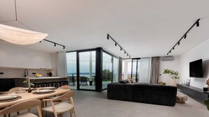 Un espacio habitable moderno con comedor, un sofá negro y un ventanal con vistas al exterior.