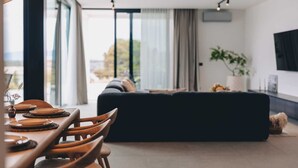 Una sala de estar moderna con un sofá oscuro, una mesa de comedor con sillas y un ventanal que ofrece vistas al exterior.