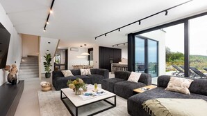 Una sala de estar moderna con sofás grises oscuros, una mesa de centro y un ventanal con vistas al exterior.