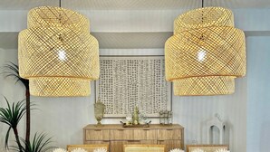 En modern inredning med två stora, flätade hänglampor, ett träbord med dekorativa föremål och en matplats med en ljus matta och vita, sfäriska prydnadsföremål.