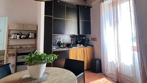 A modern kitchen with wooden beams, a dining area with a round table, and a large window with curtains. - Galileo Apartment (Firenze)