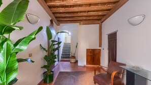 A hallway with a wooden ceiling, a staircase, a door, a glass table, and a brown leather chair. - Galileo Apartment (Firenze)
