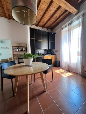 A modern kitchen with black cabinets, a round wooden table with chairs, a potted plant, and a large window with curtains. - Galileo Apartment (Firenze)