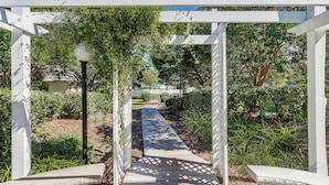 Un chemin de jardin bordé d’une pergola blanche à motifs de treillis, entouré de verdure et surplombé par un ciel dégagé.