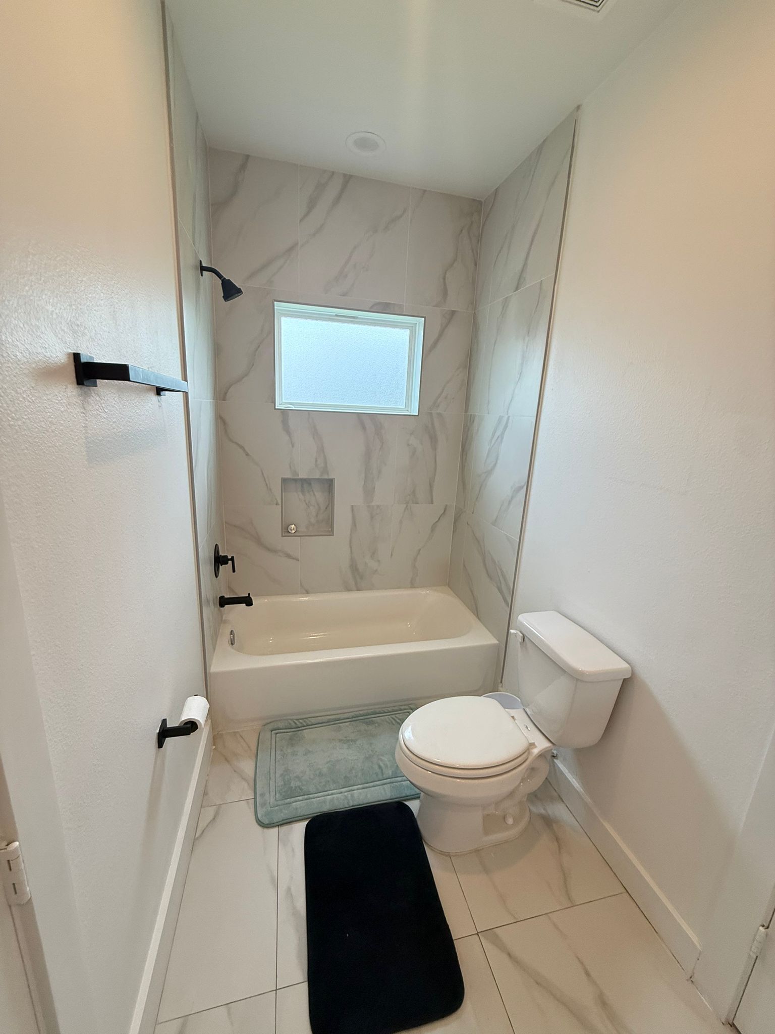 A compact bathroom with a bathtub, toilet, and a small window.