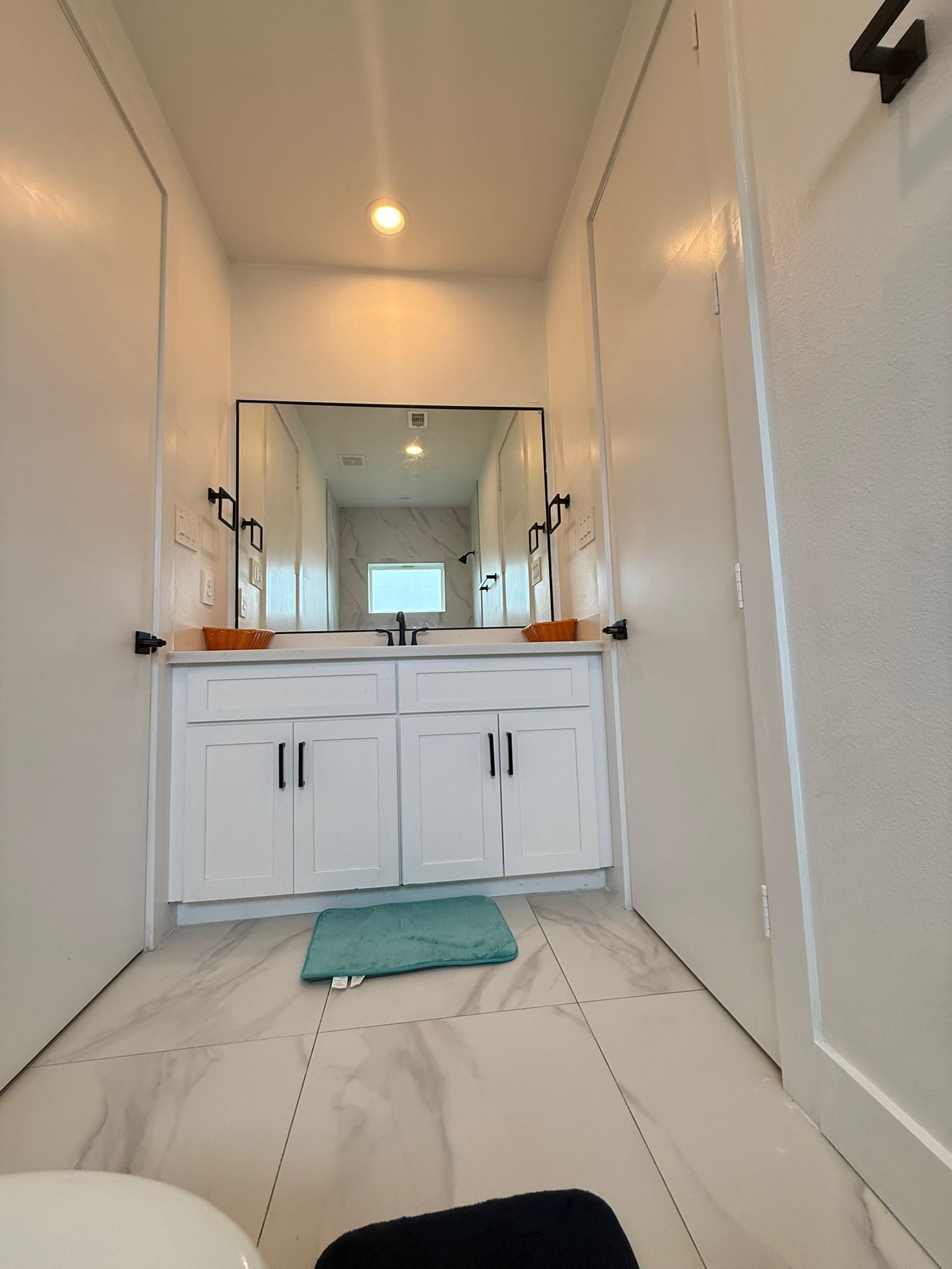 Un couloir menant à une salle de bain avec des meubles blancs, un miroir et un tapis turquoise sur le sol.