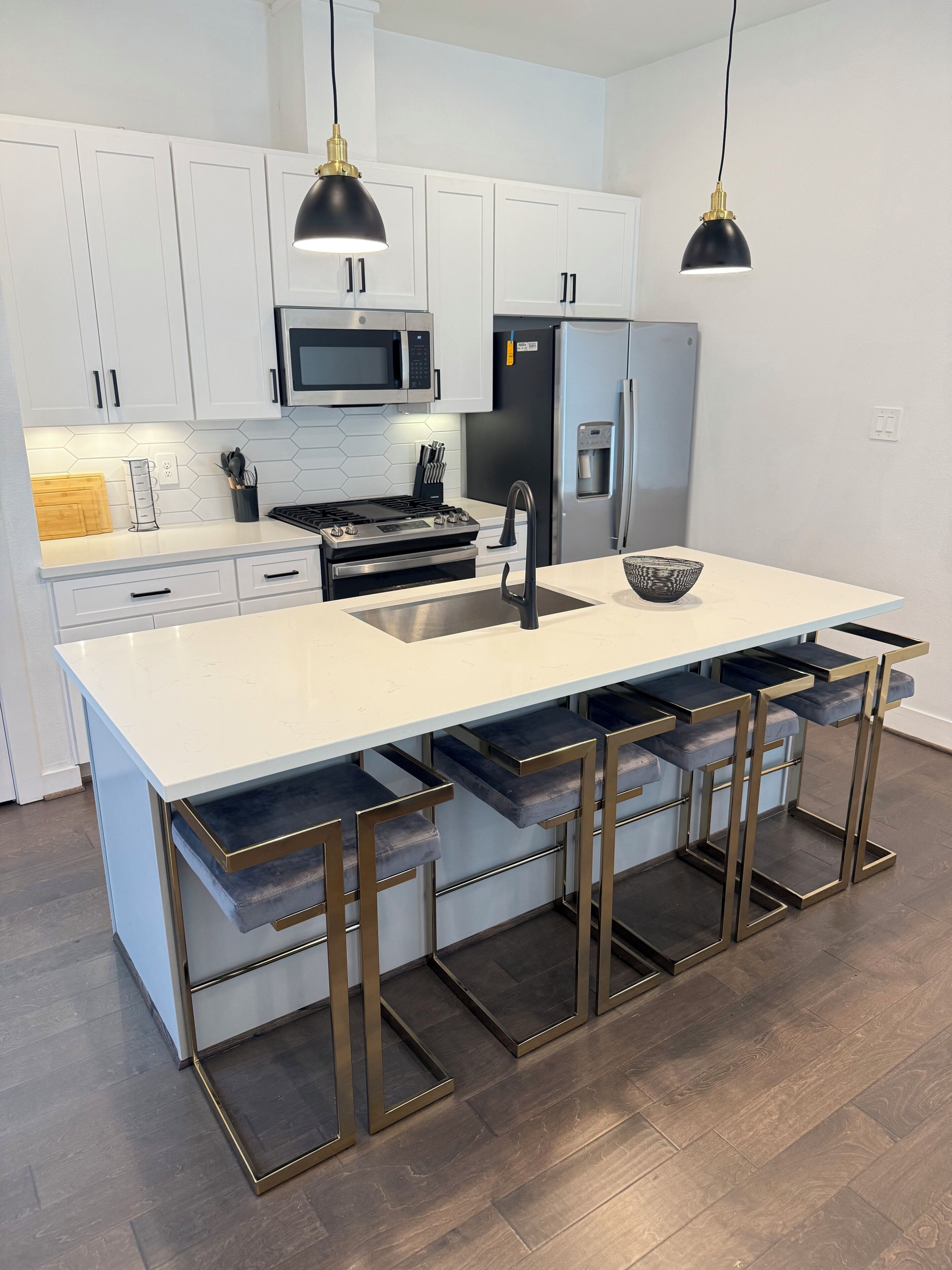 Una cocina moderna con gabinetes blancos, electrodomésticos de acero inoxidable y una isla central con taburetes de bar.