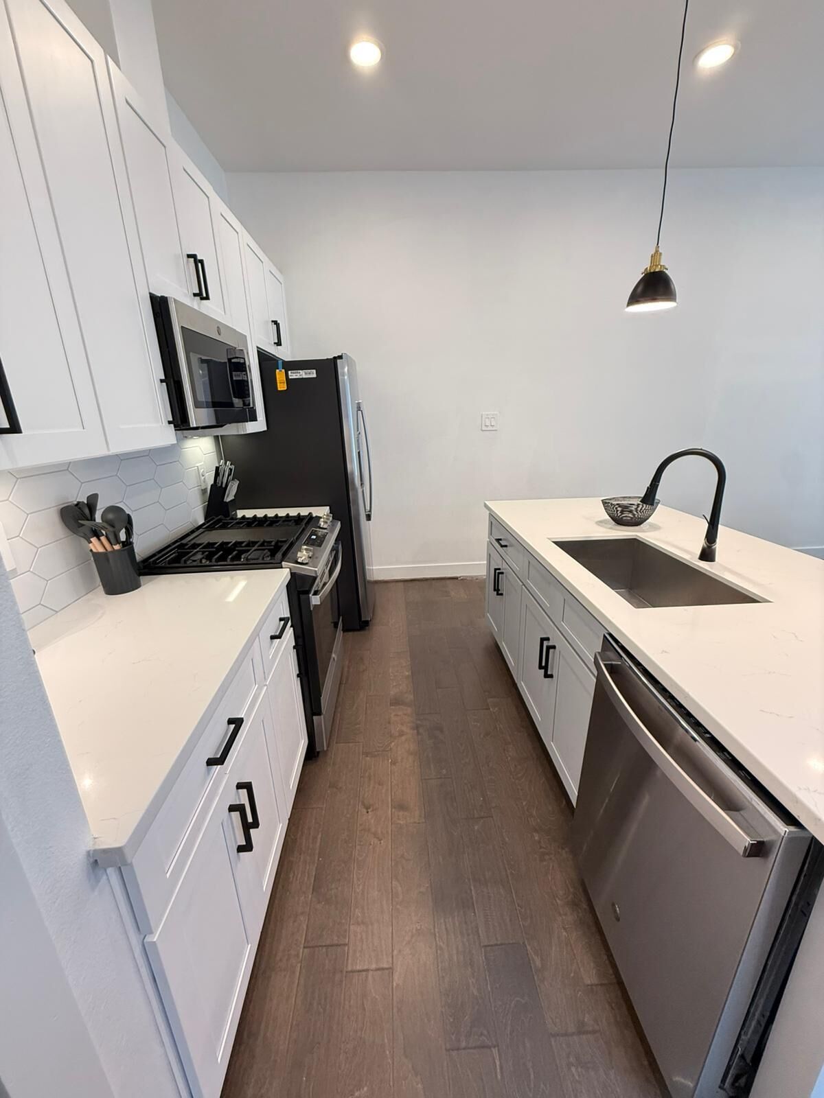 Una cocina moderna con armarios blancos, un refrigerador negro, un microondas, una estufa y un lavavajillas.