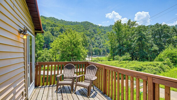 A wooden deck with two Adirondack chairs and a table, overlooking a lush green landscape and hills. - 1 Mi to Hatfield-McCoy Trails: Apt in Matewan (Matewan)