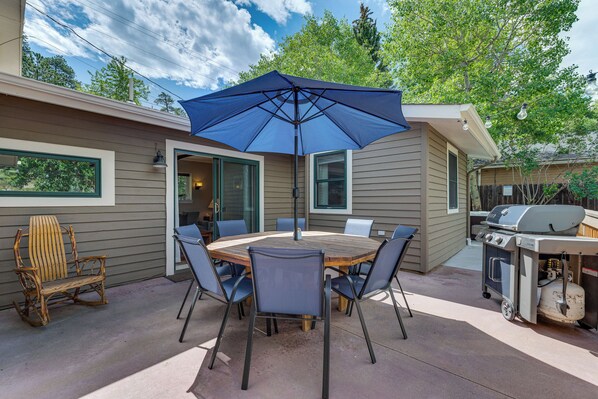 An outdoor patio with a round table and chairs, a blue umbrella, and a grill. - Cozy Hot Tub & Fireplace - Estes Park Riverfront (Estes Park)