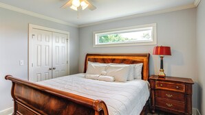 Une chambre à coucher avec un lit en bois, du linge de lit blanc, une table de chevet avec une lampe et une fenêtre donnant sur un paysage verdoyant.