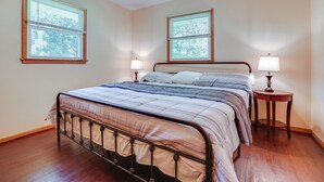 Un dormitorio con una cama, dos mesitas de noche y dos ventanas con persianas.