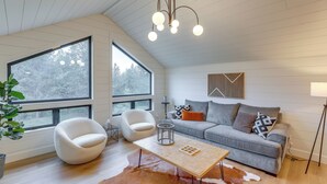 A modern living room with a large window, a white chair, a gray sofa, and a wooden coffee table. - Cabin on 28 Acres: Hike & Fish in Flathead Valley! (Marion)
