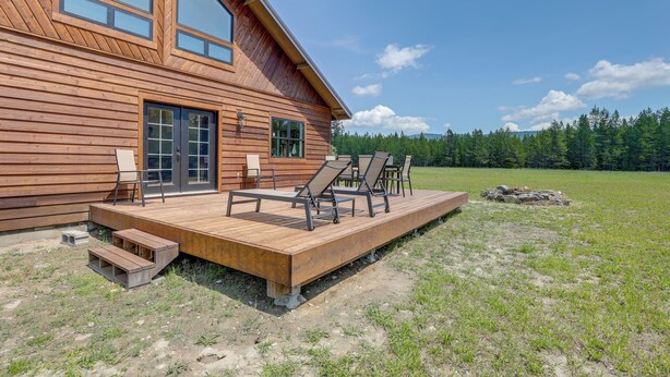 A wooden cabin with a deck, outdoor seating, and a view of a forest. - Cabin on 28 Acres: Hike & Fish in Flathead Valley! (Marion)