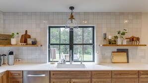 A modern kitchen with a large window, wooden cabinets, and a stainless steel dishwasher. - Cabin on 28 Acres: Hike & Fish in Flathead Valley! (Marion)