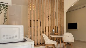 Ein modernes Zimmer mit einem weißen Kühlschrank, einer Holzwand, zwei weißen Stühlen, einem kleinen runden Tisch und einem flachbildfernseher, der an der Wand befestigt ist.