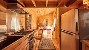 A wooden cabin interior with a kitchen featuring a stove, sink, and refrigerator.