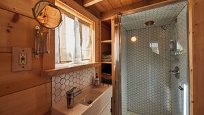 A wooden cabin bathroom with a sink, mirror, and shower.