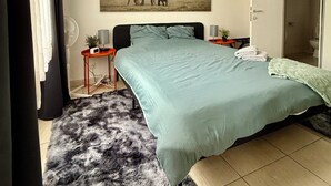Een slaapkamer met een groot bed, een aan de muur hangend beeld van olifanten, een klein tafeltje met een lamp en een zacht vloerkleed.