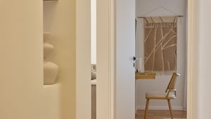 Ein Flur, der in einen Raum führt, mit einem hölzernen Stuhl, einem kleinen Tisch und einem Wandteppich.