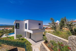 A modern two-story house with a swimming pool, stone retaining wall, and a view of the surrounding landscape. - Luxury villa 45° with infinity pool (Punat)