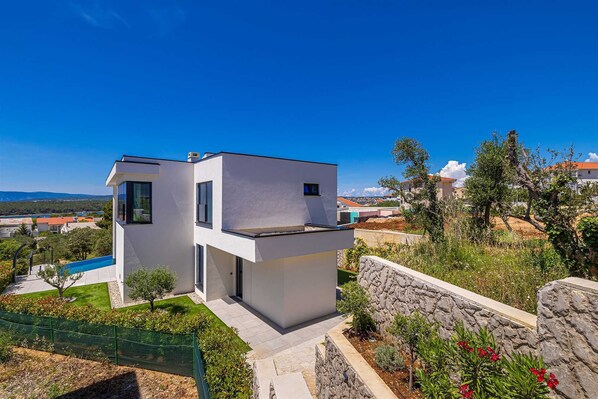 A modern two-story house with a swimming pool, stone retaining wall, and a view of the surrounding landscape. - Luxury villa 45° with infinity pool (Punat)