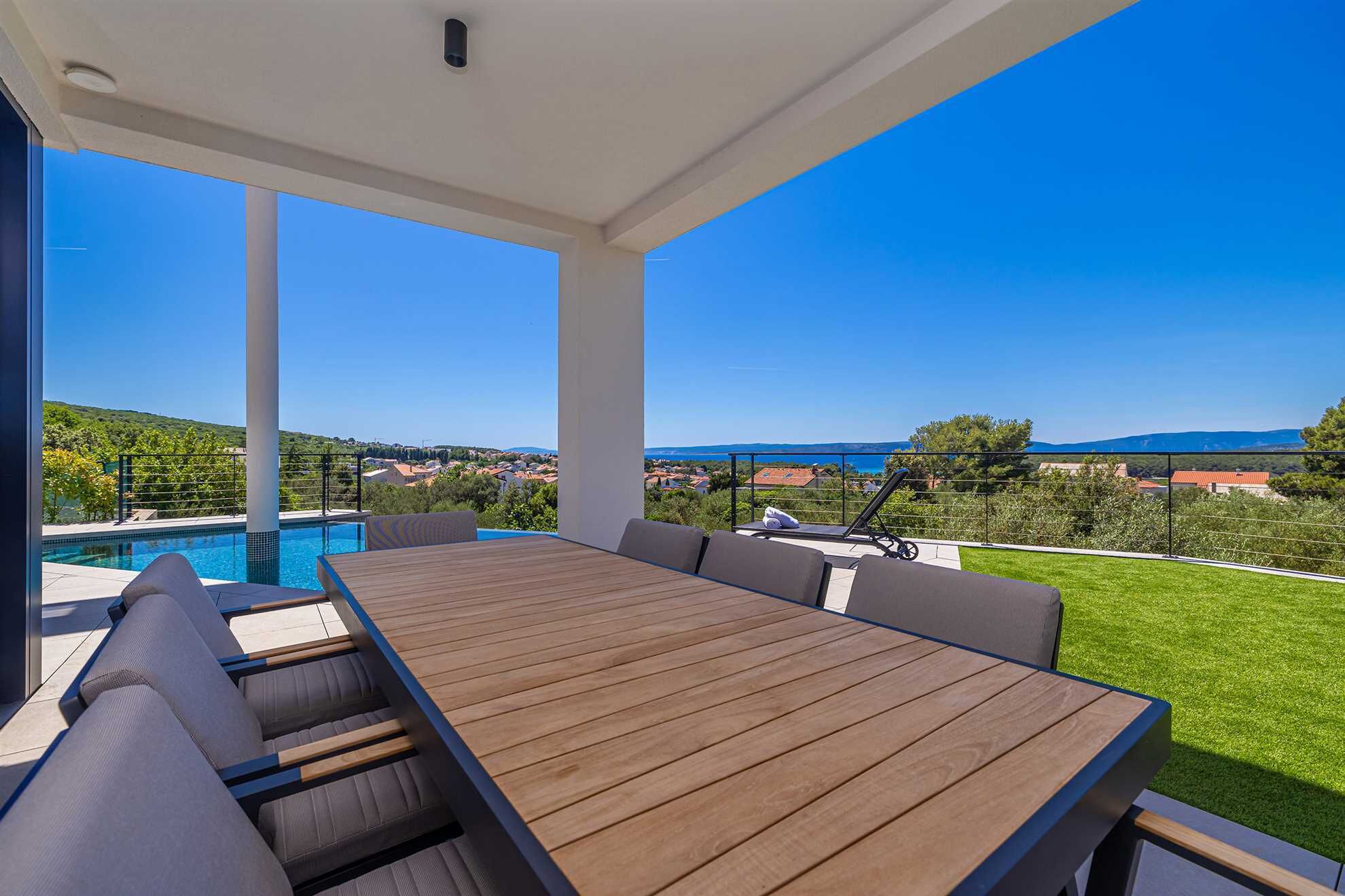 Un espacio al aire libre techado con piscina, una mesa de madera y sillas, con vistas a un paisaje pintoresco.