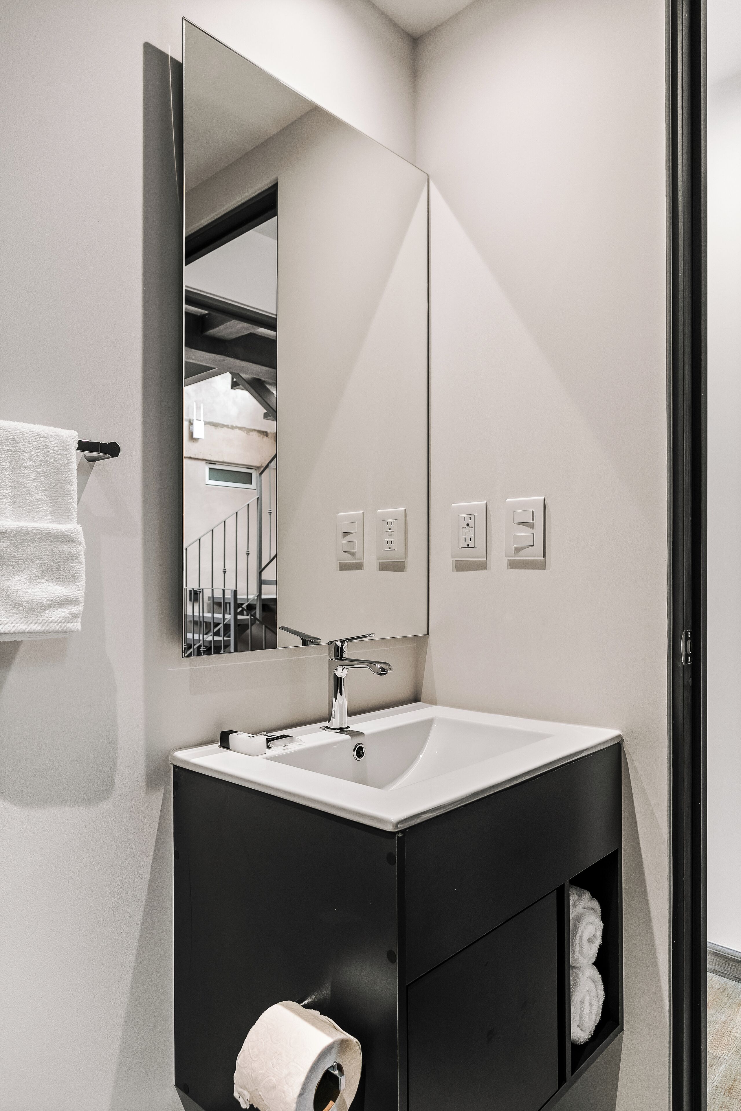 A modern bathroom with a white sink, black vanity, a large mirror, and a towel rack.
