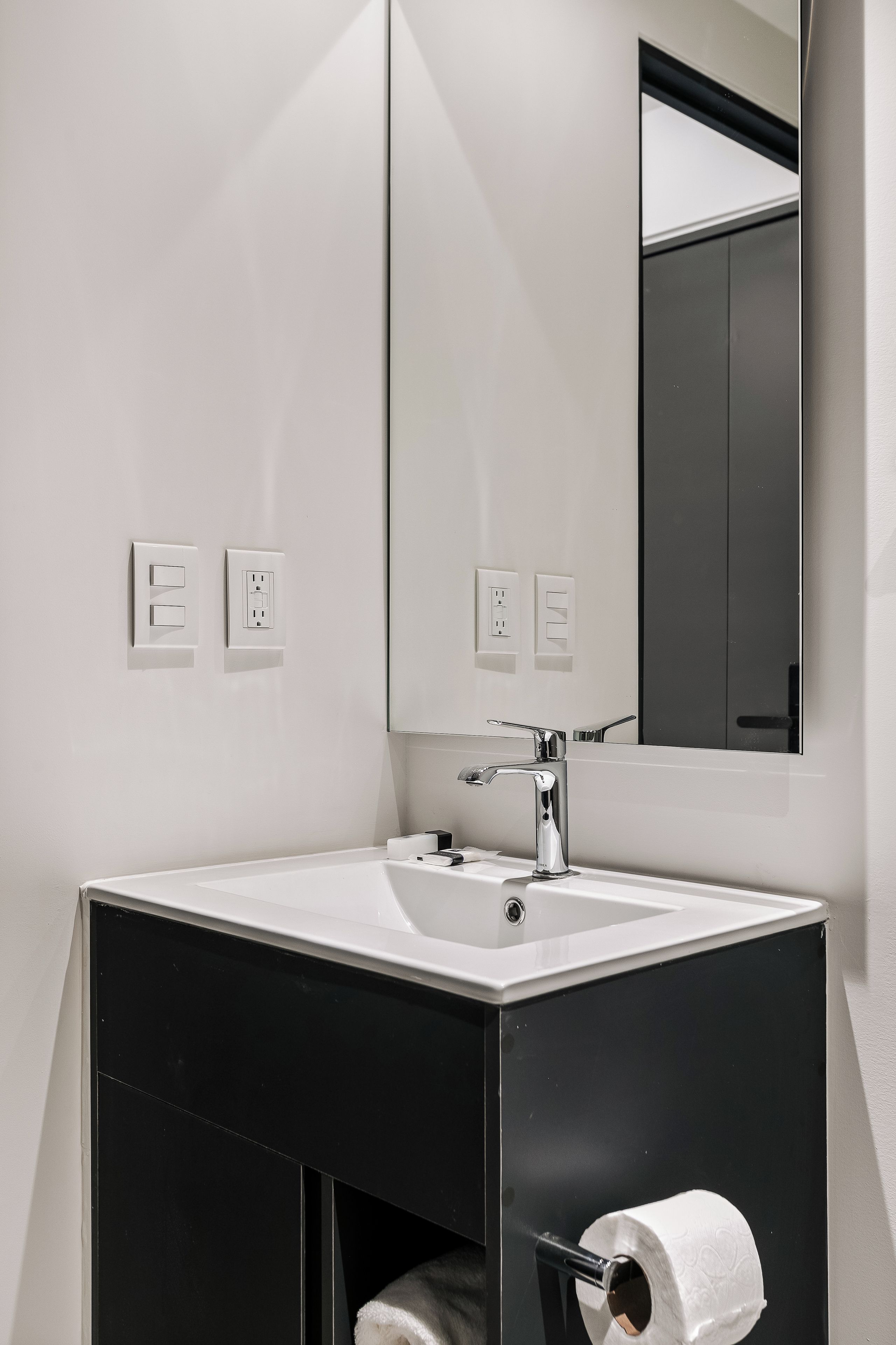Une salle de bain moderne avec un lavabo blanc, un miroir et deux interrupteurs sur le mur.