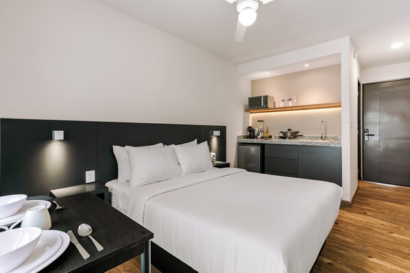 Een hotelkamer met een bed, een kleine keuken, een eettafel met borden en bestek, en een deur.