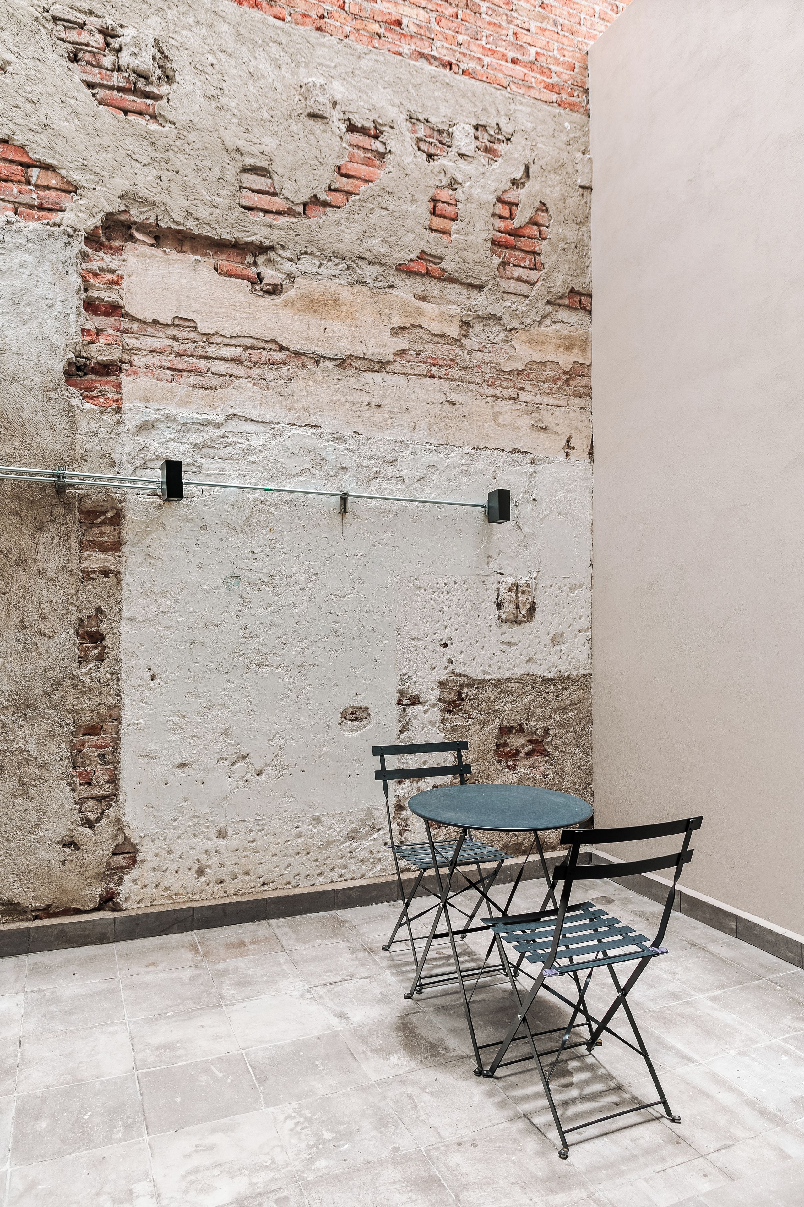 A room with a brick wall, a metal bar, and a small table with a chair.