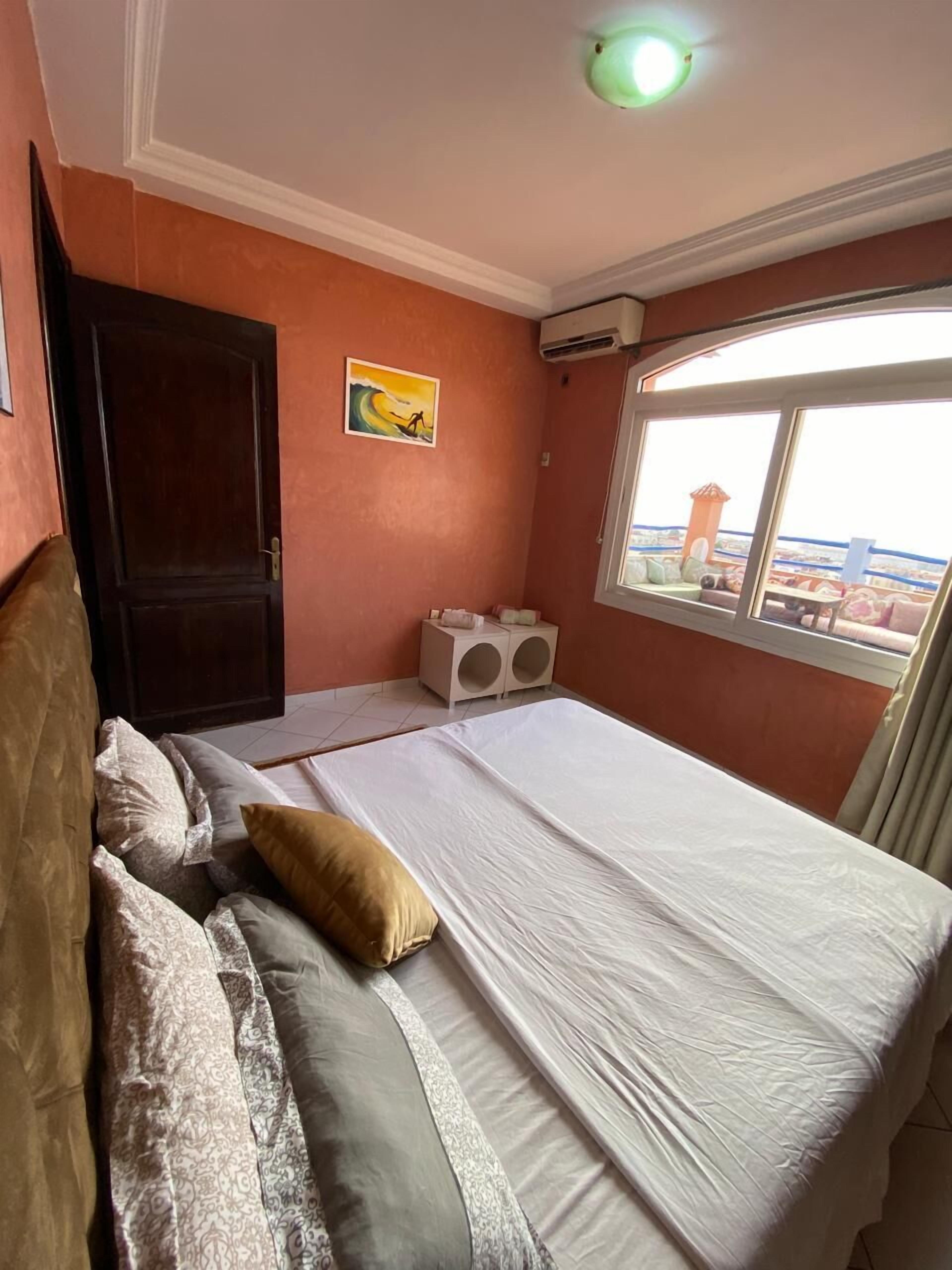 Un dormitorio con cama, almohadas, un cuadro, un equipo de aire acondicionado y una ventana con vistas.