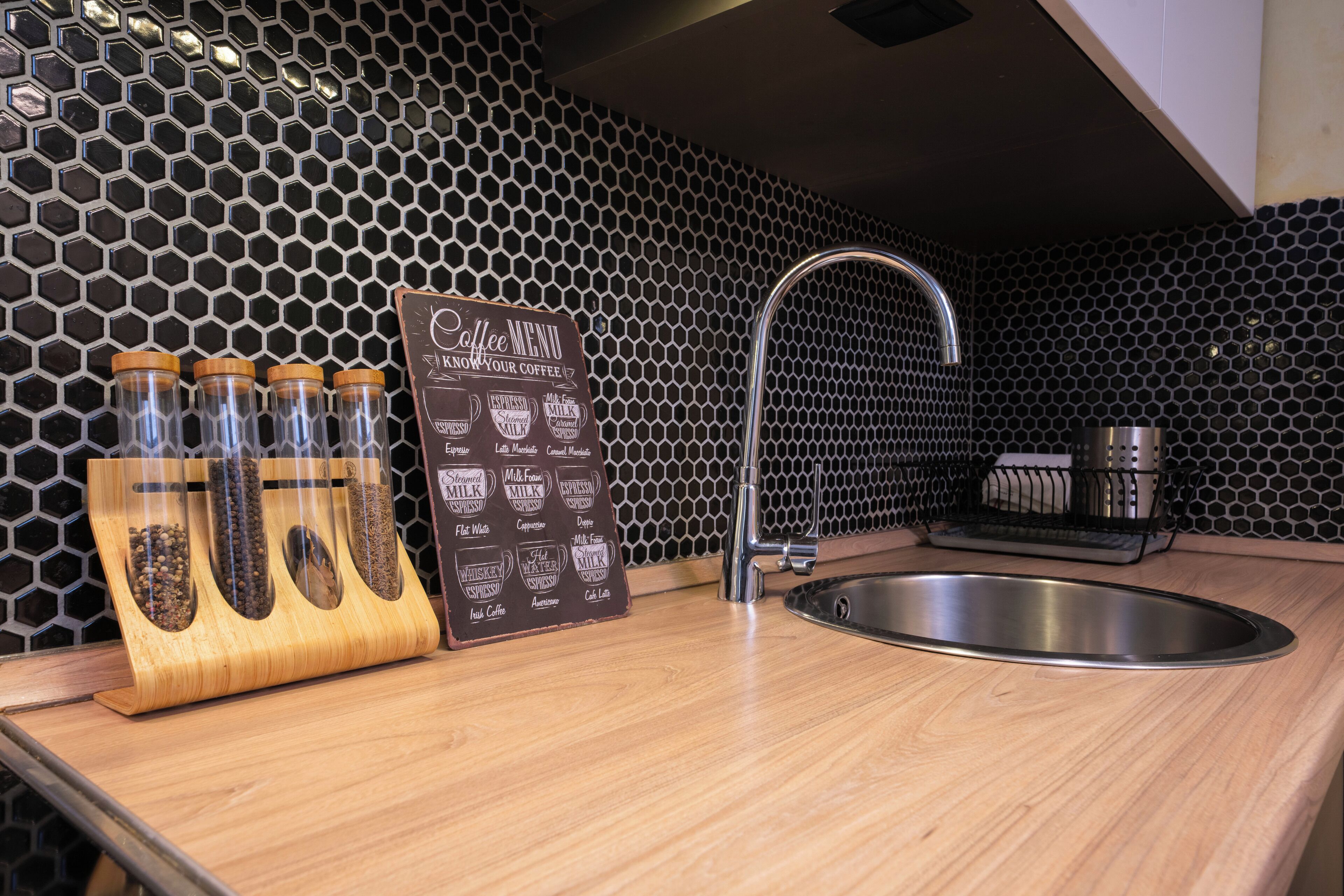Een keuken met een honingraatachterwand, een bord met koffie aanbiedingen, een roestvrijstalen spoelbak en een houten kruidenrek.