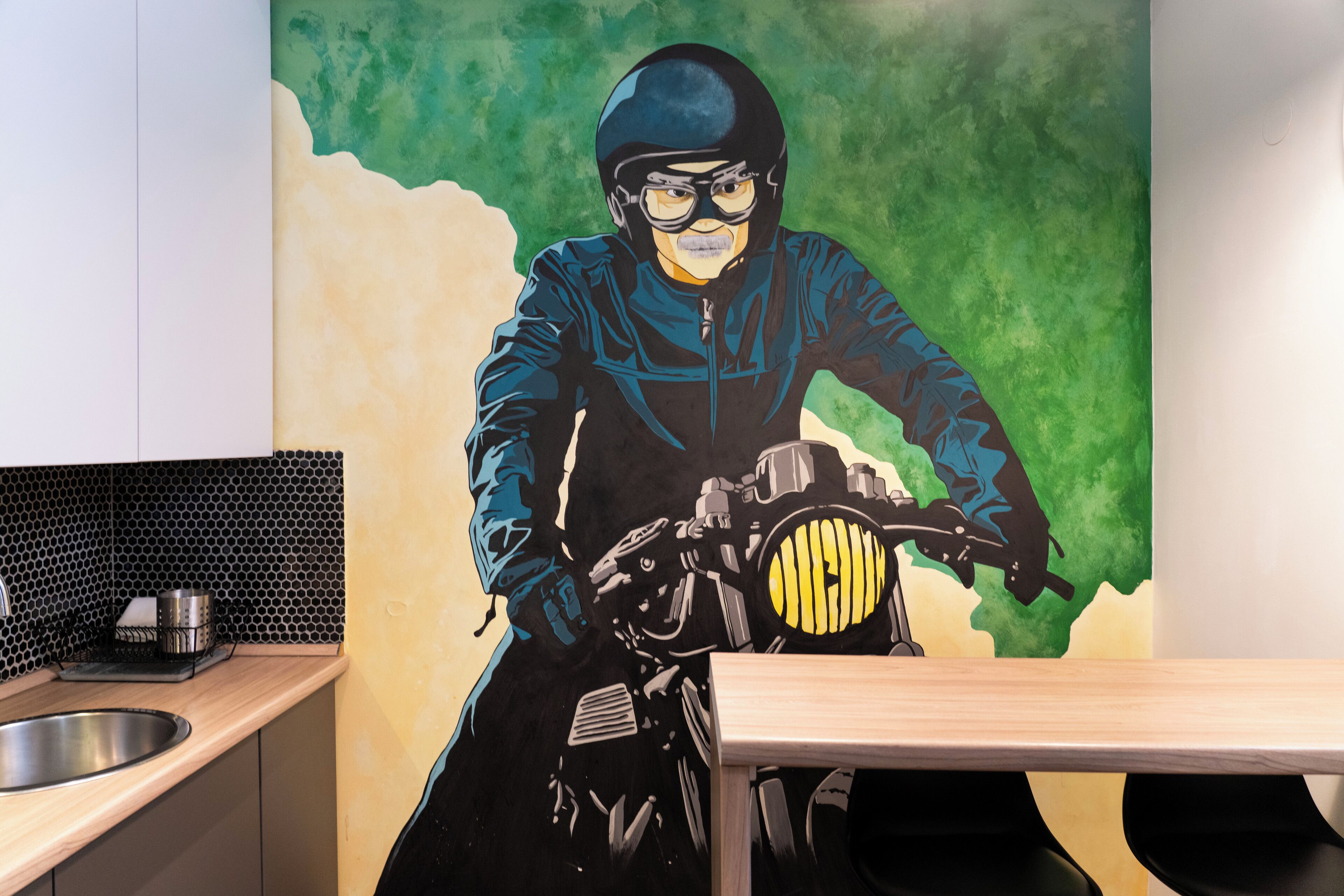 Eine Küche mit Wandgemälde einer Person auf einem Motorrad, einem Spülbecken und einem Holztisch.