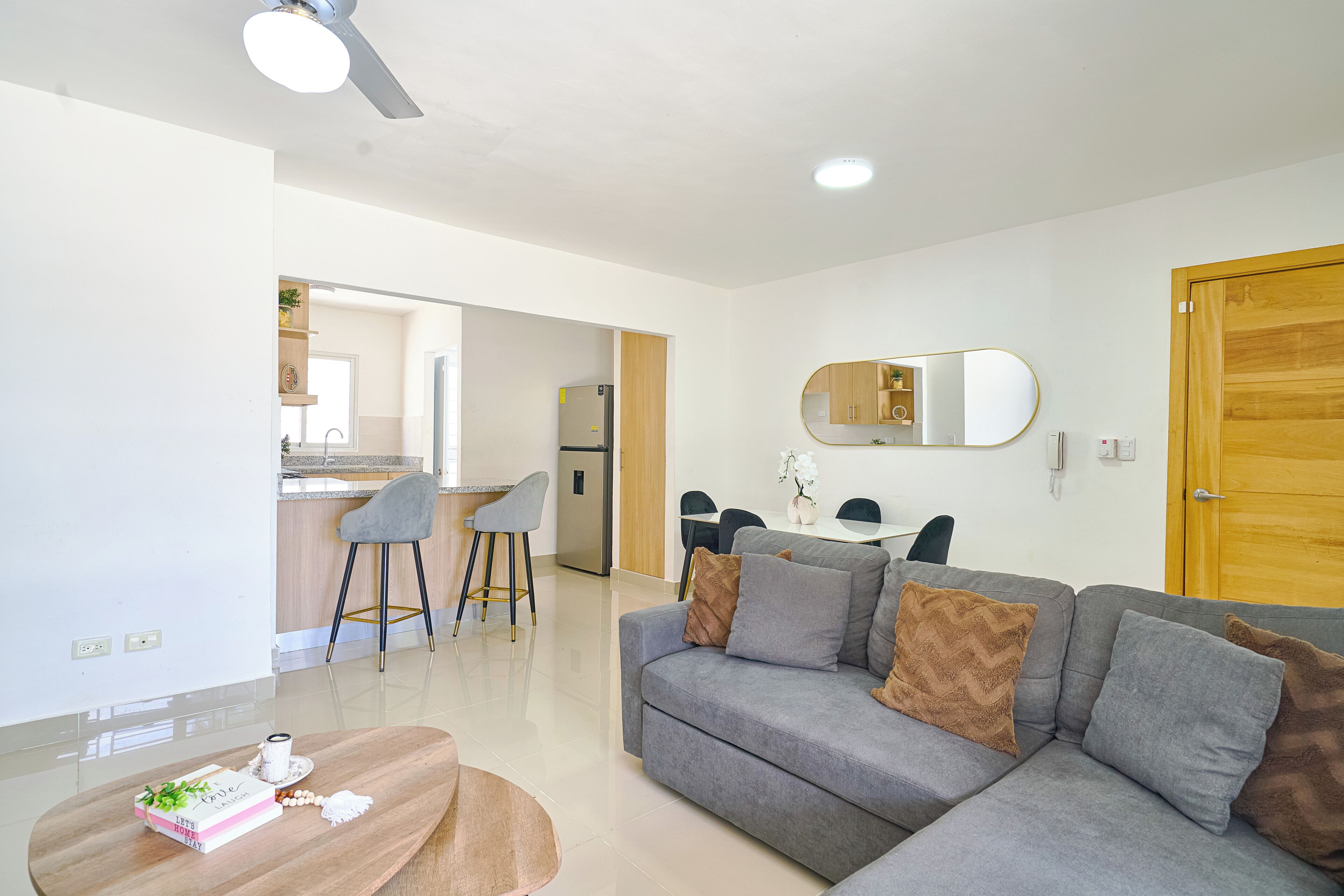 A modern living room with a grey sofa, a wooden dining table, and a kitchen in the background.