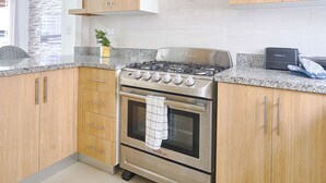 A modern kitchen with wooden cabinets, a stainless steel stove, and granite countertops. - Charming 3-bedroom apartment with Wi-Fi, AC in welcoming Santo Domingo Este. (Santo Domingo Este)