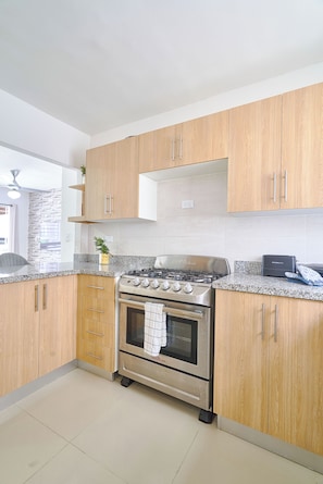 A modern kitchen with wooden cabinets, a stainless steel stove, and granite countertops. - Charming 3-bedroom apartment with Wi-Fi, AC in welcoming Santo Domingo Este. (Santo Domingo Este)