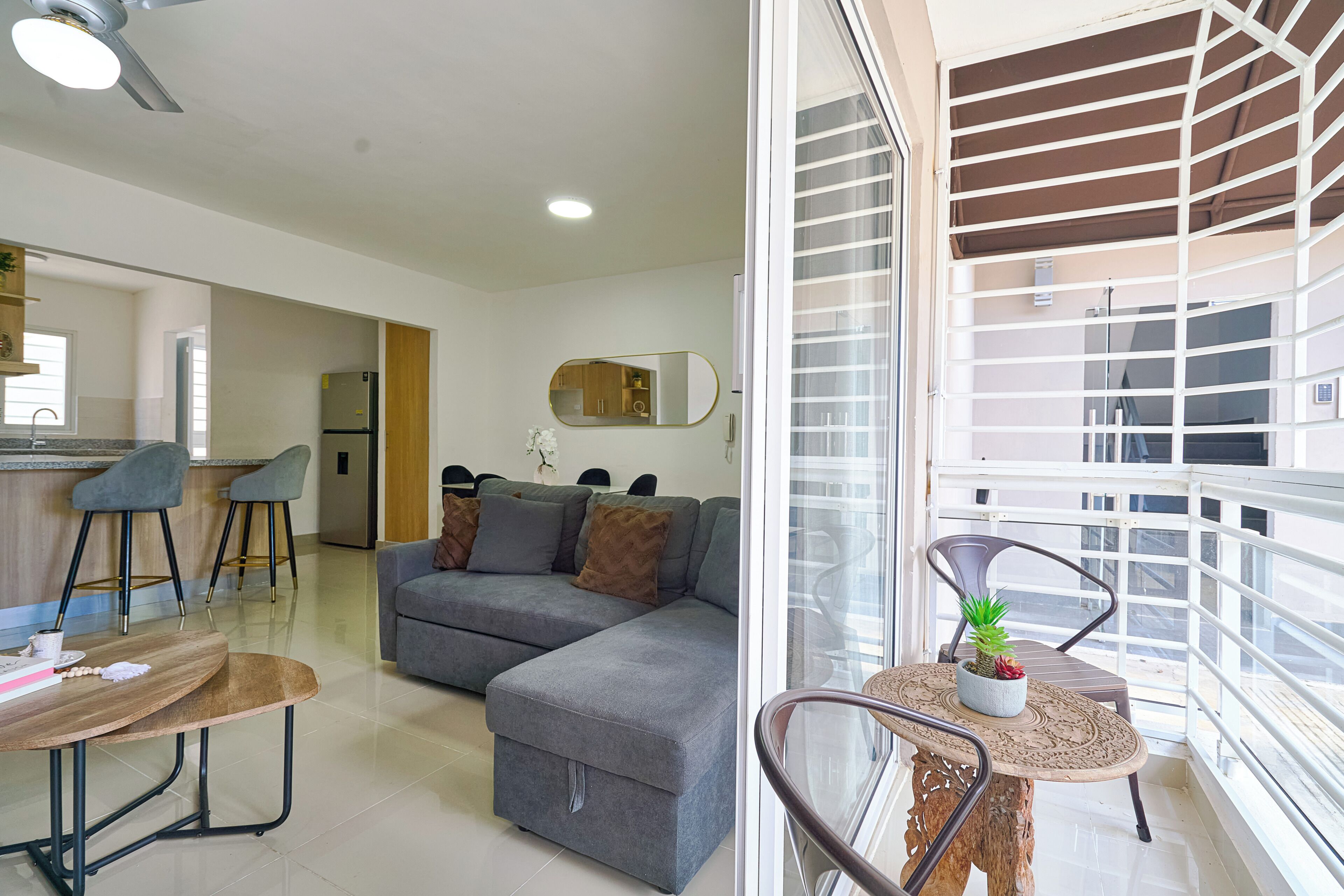 Un salon moderne avec un canapé gris, un coin repas doté d’une table ronde et un balcon avec une balustrade.