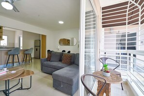 Una sala de estar moderna con un sofá gris, un comedor con una mesa redonda y un balcón con barandilla.